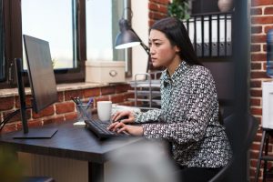 wanita sedang fokus bekerja di depan komputer dengan ekspresi serius