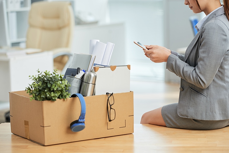 woman suit sitting desk office with belongings box using smartphone